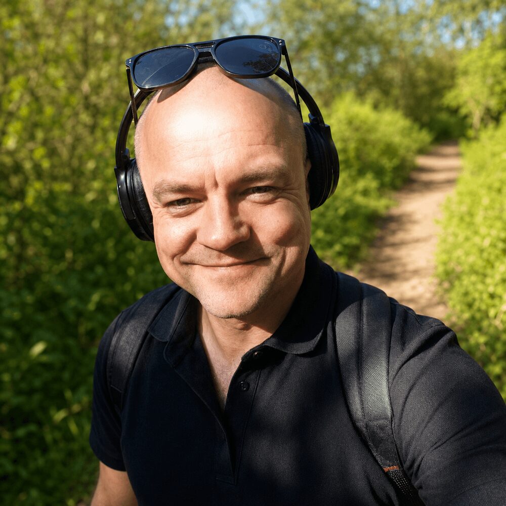 Portrait of Ágúst Ævar Guðbjörnsson, smiling outdoors with headphones on and sunglasses resting on top of the head
